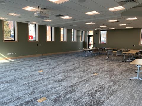 Image of the full community room with tables and chairs in front of the far wall.